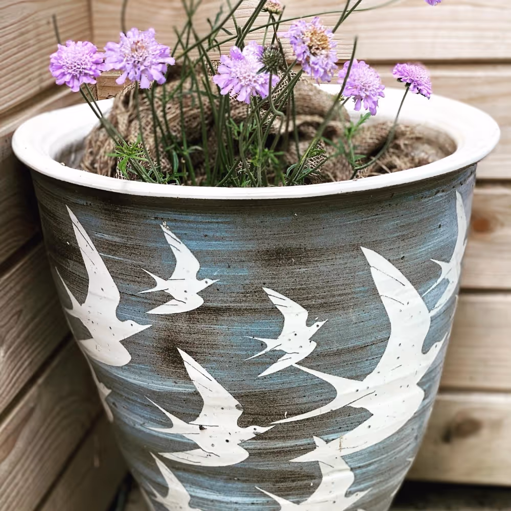 A large stoneware planter with thrift planted in the top
