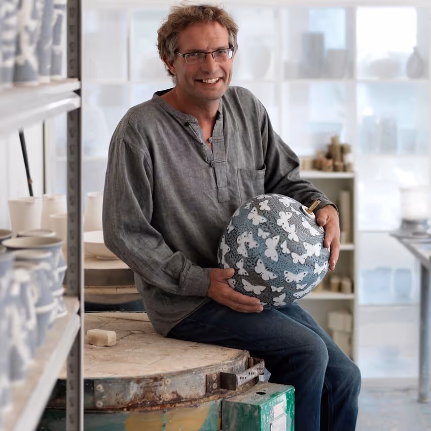 A potter holding one of his grey-blue glazed bowls