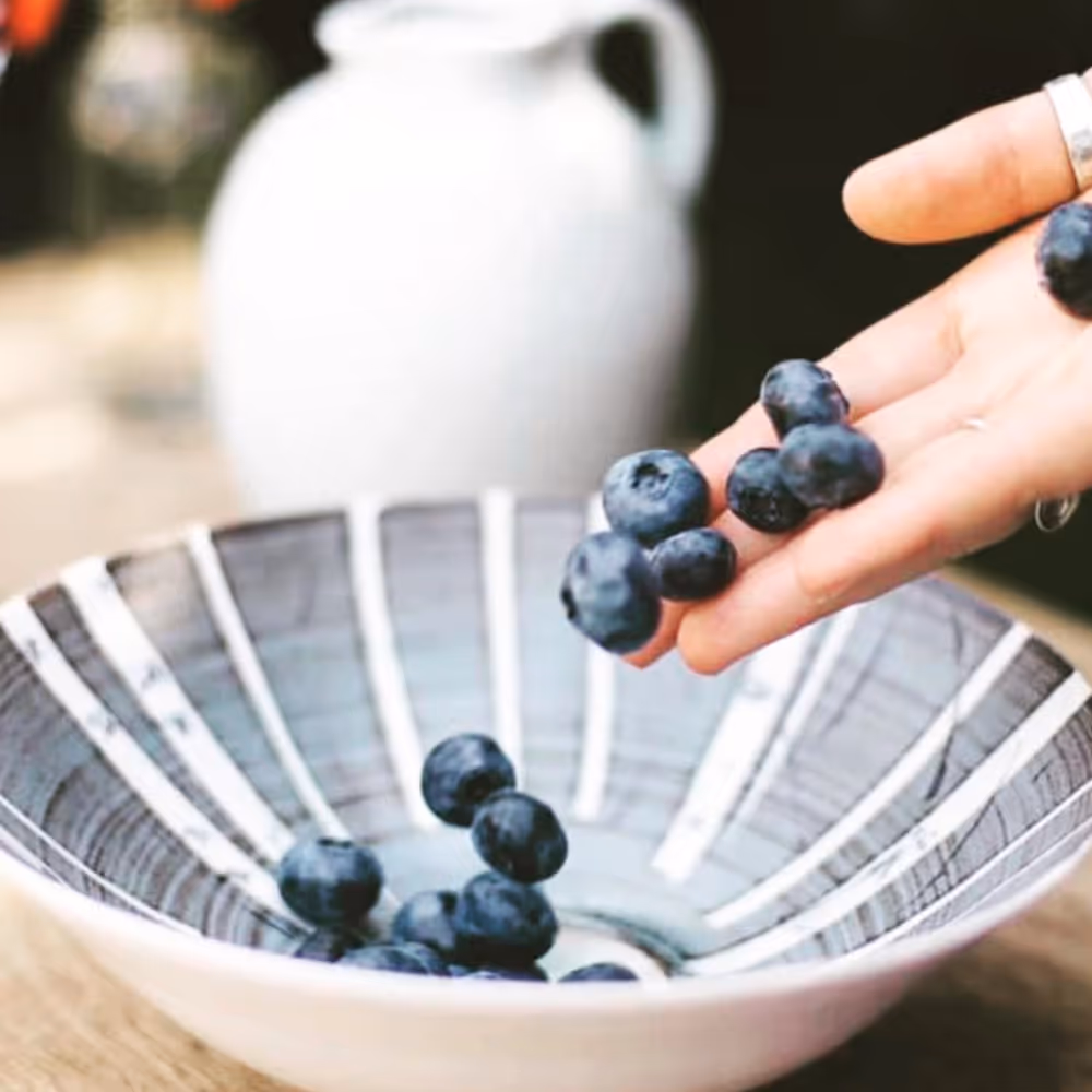 A blue-grey glazed bowl being filled with blueberries
