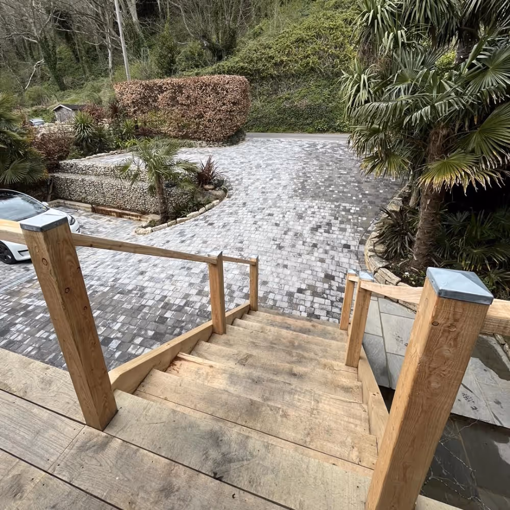 Outside wooden steps leading down to a grey paved driveway