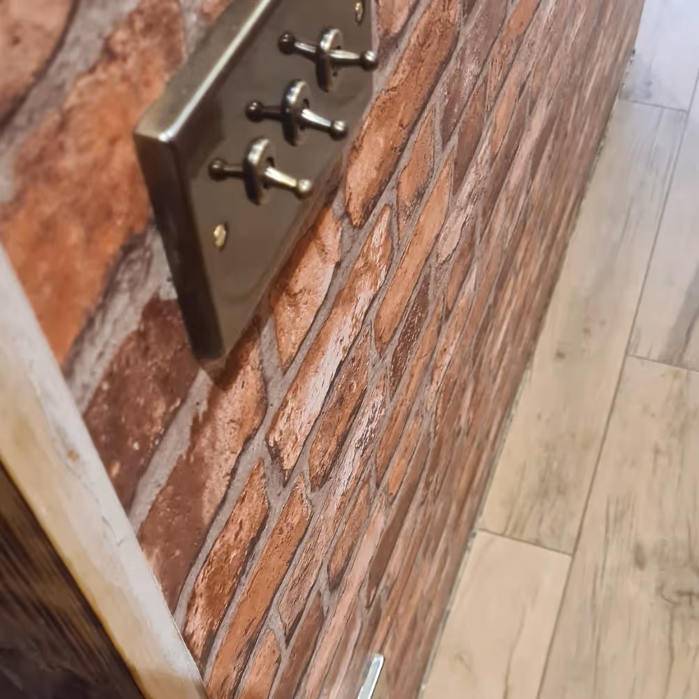 A satin nickel light switch on a faux brick wallpaper