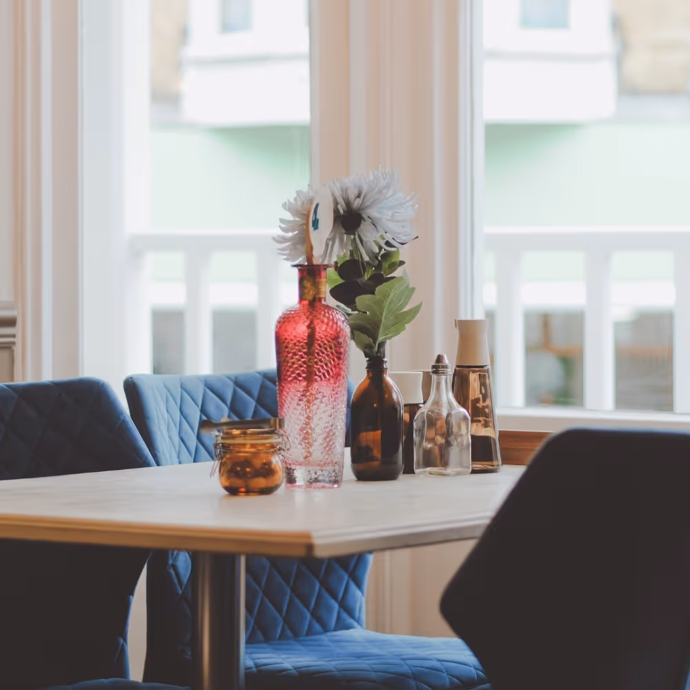 A cafe table with condiments and a pretty pink glass vase