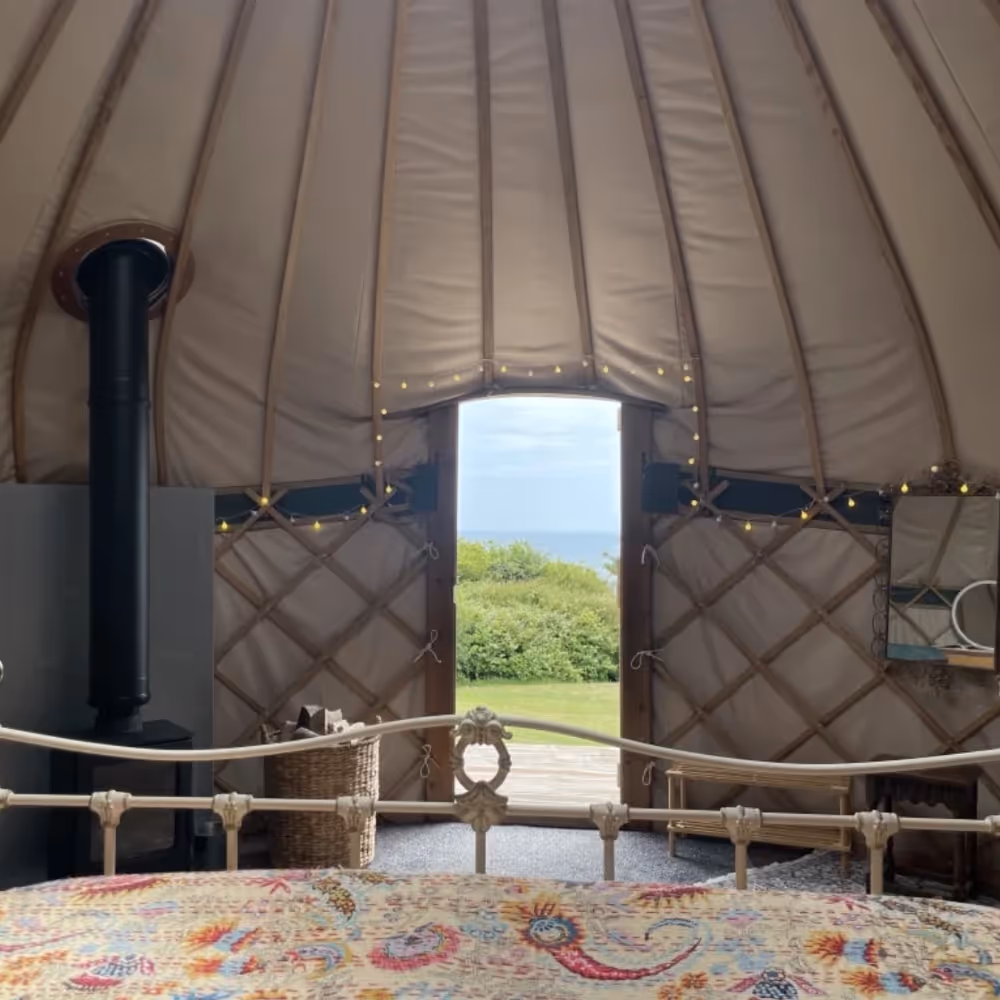 A view to the sea from a bed inside a glamping yurt