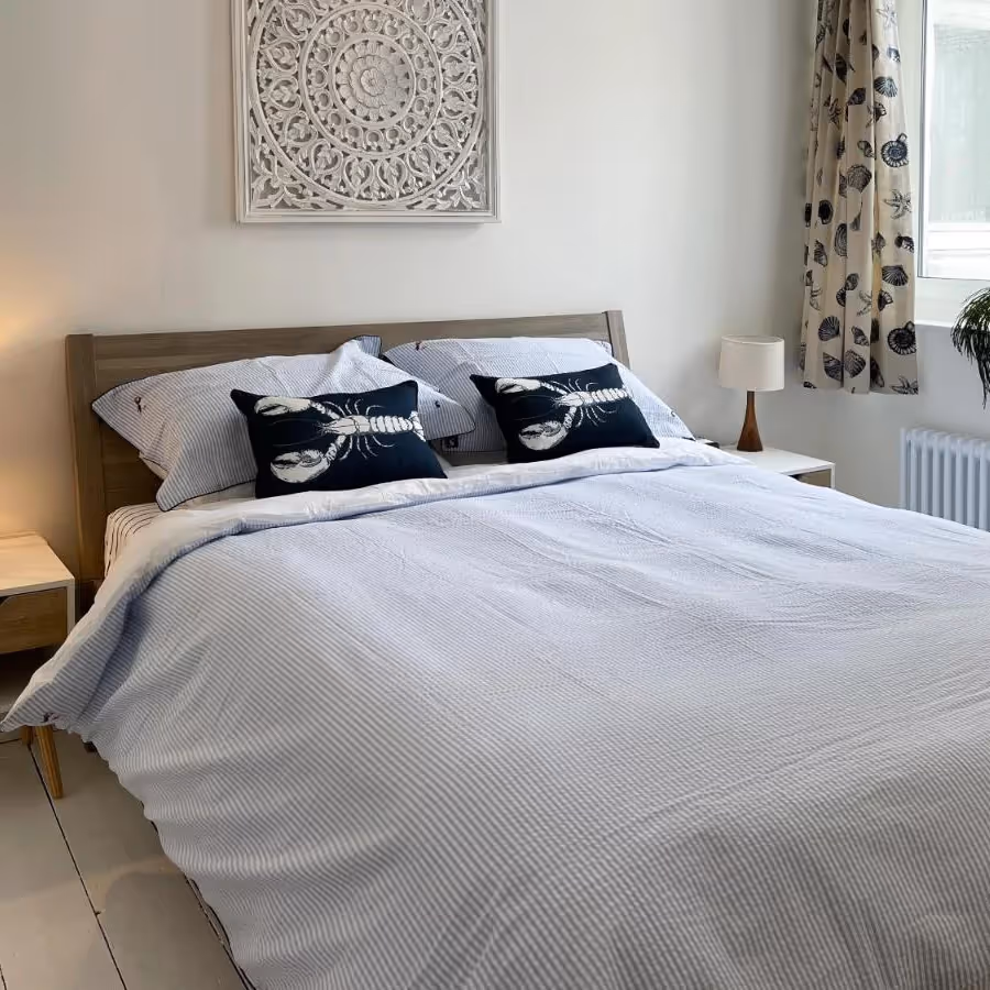 A bedroom with white bedlinen and coastal cushions