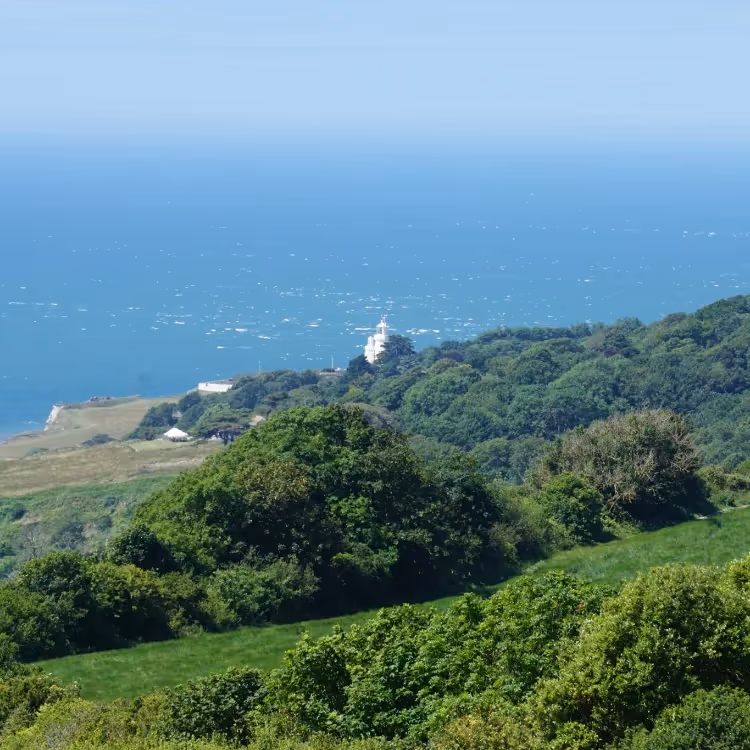 A high up view across fields to the sea and a lighthouse beyond