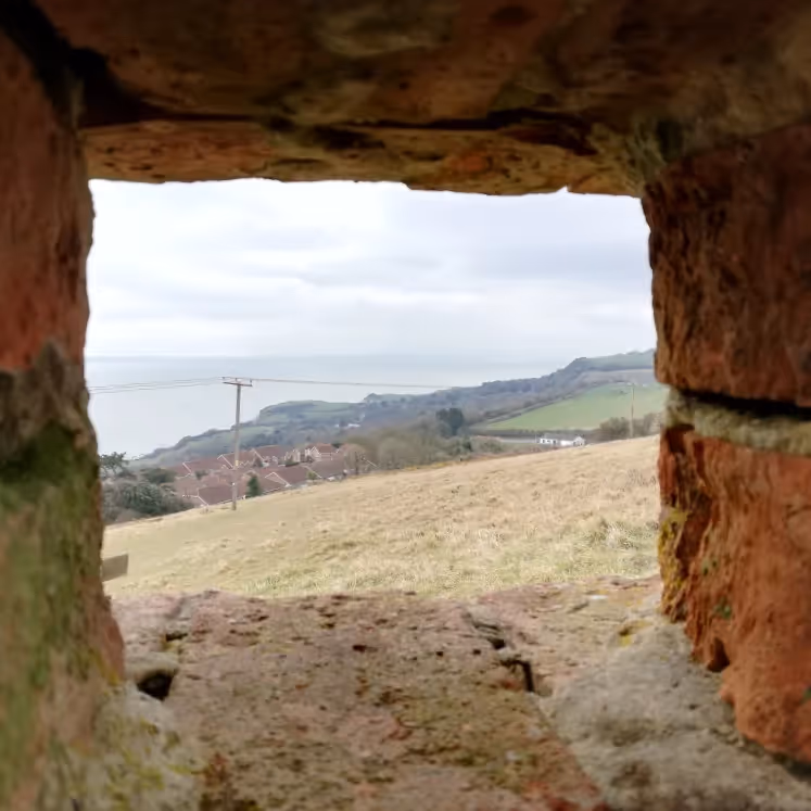 Looking through a derelict brick opening to a sea view beyond
