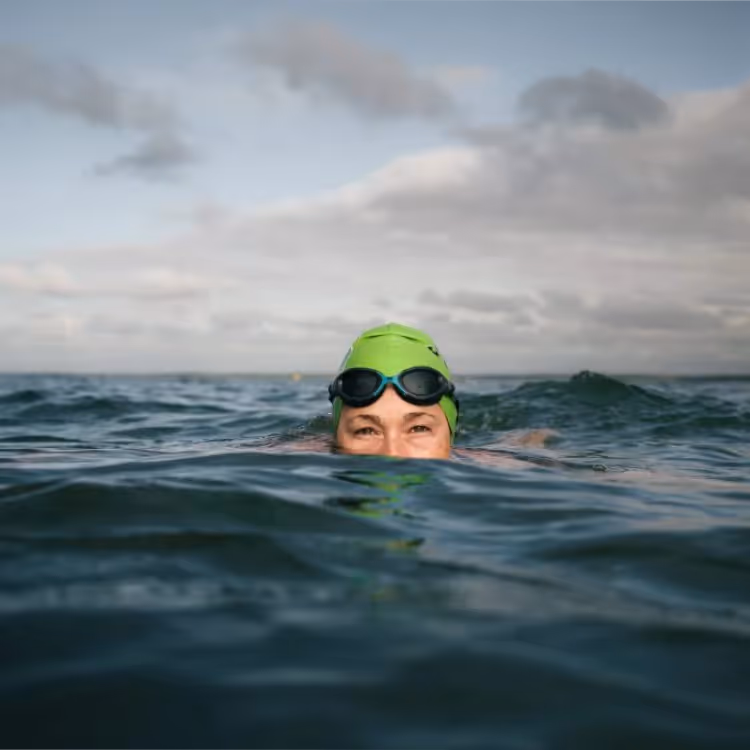 A lady in the sea wearing a green swimming cap