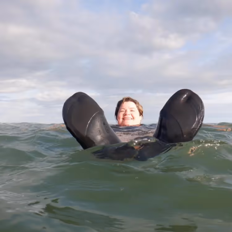 A lady in a wet suit floating in the sea