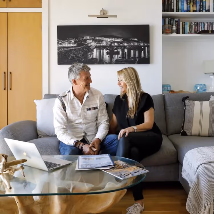 A man and woman sitting on a grey corner sofa