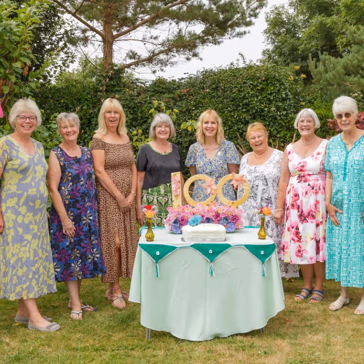 A group of ladies stood around a table in a garden