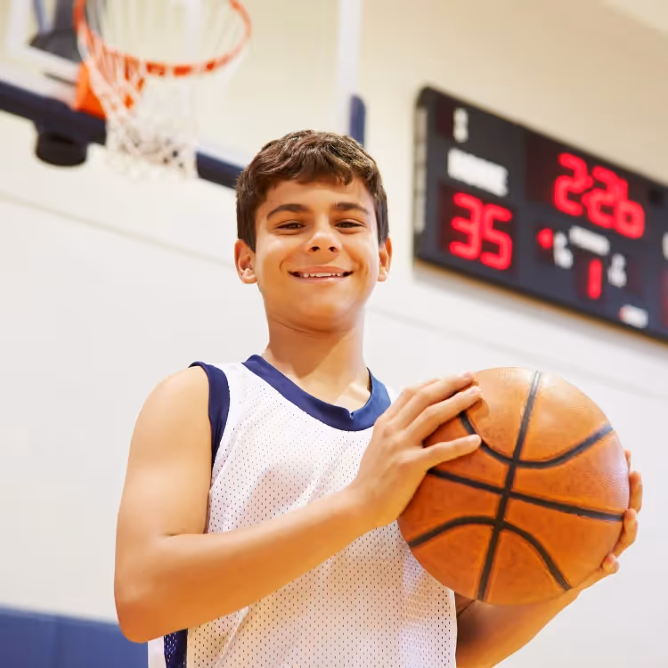 A kid holding a basketball in front of a score board