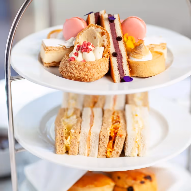 A three tier cake stand with cakes and finger sandwiches