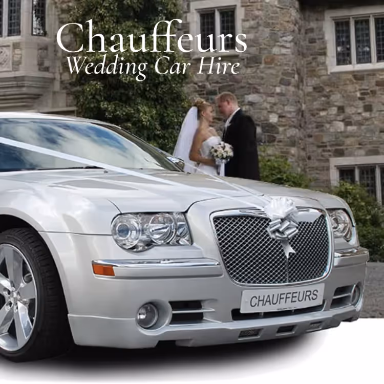 A bride and groom kissing by their wedding car outside a mansion