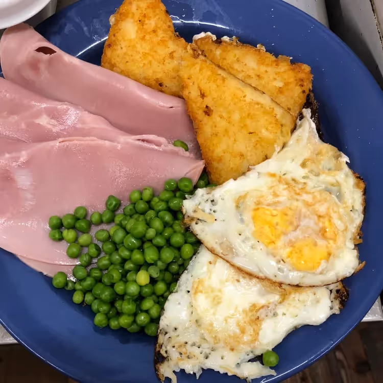 A plate of ham, eggs, peas and hashbrowns