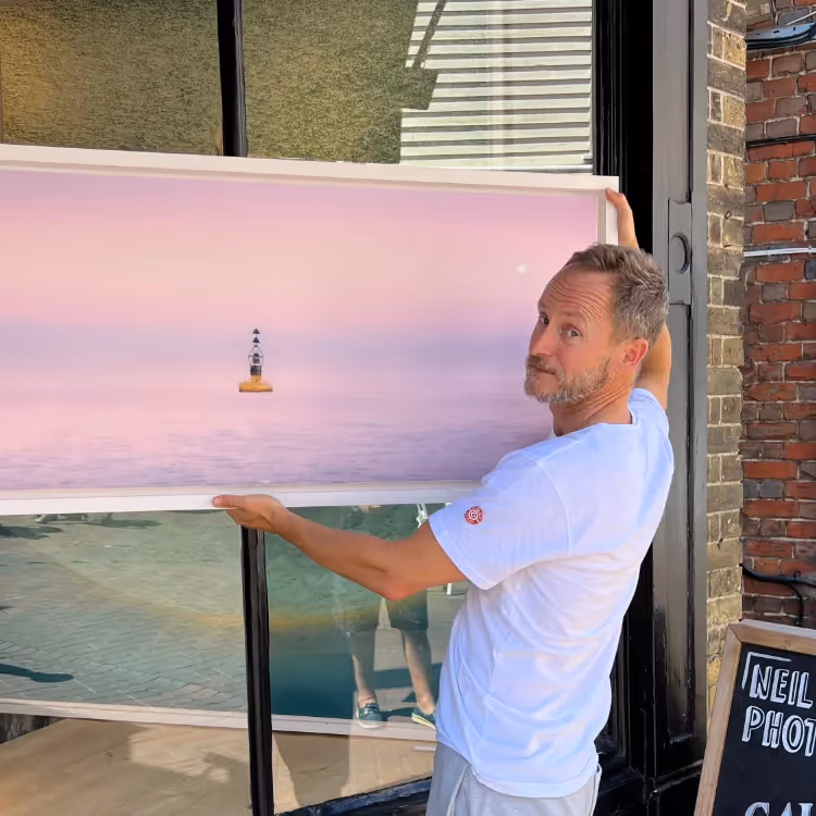 A photographer holding a framed photo of a coastal buoy