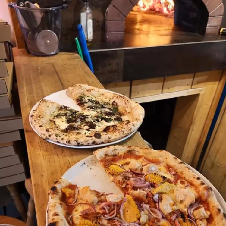 Two pizzas in front of a pizza oven