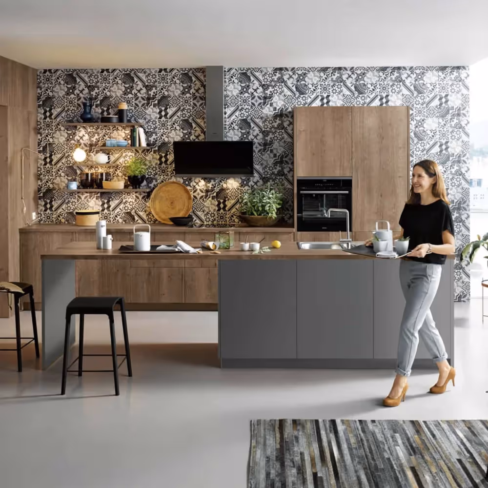 A lady walking through a modern grey and walnut kitchen