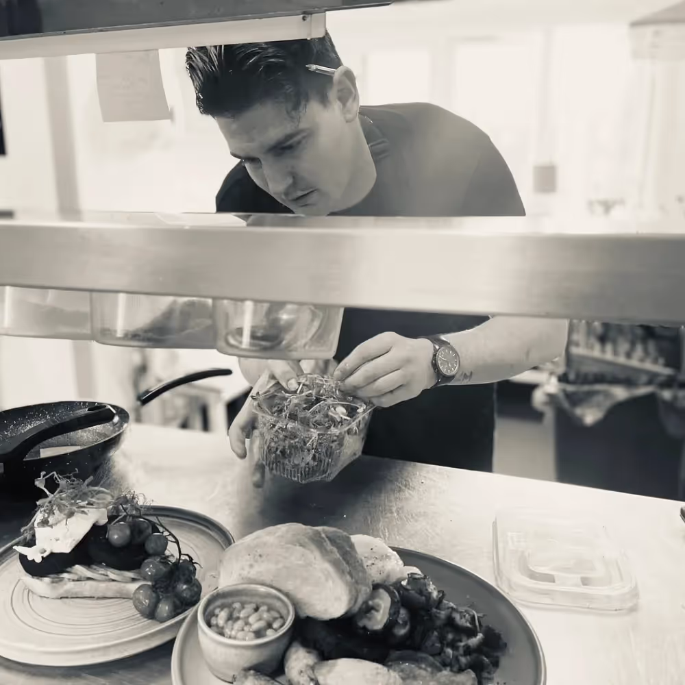 A chef serving food onto a plate in a restaurant kitchen