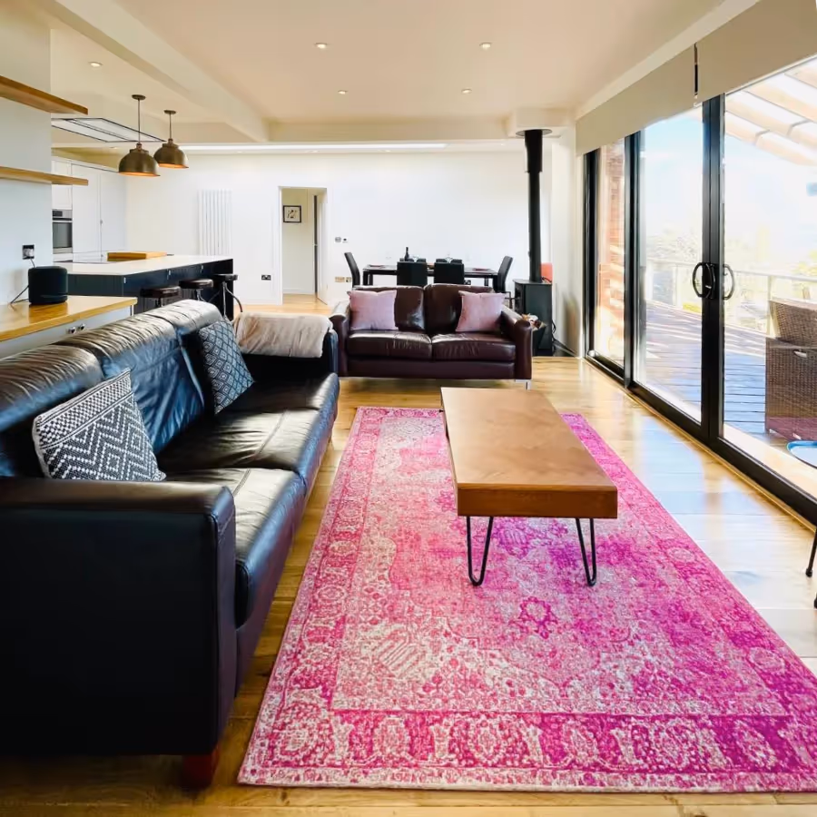 A large living room with brown leather sofas and a bright pink rug