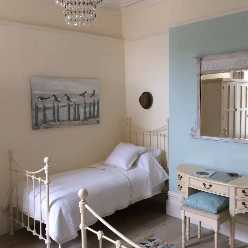 A bedroom with two metal bedsteads and a cream dressing table