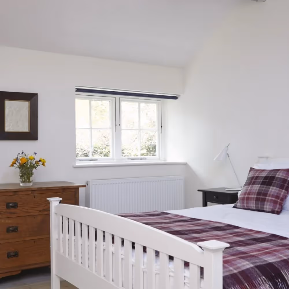 A bedroom with a white bedframe and teak chest of drawers