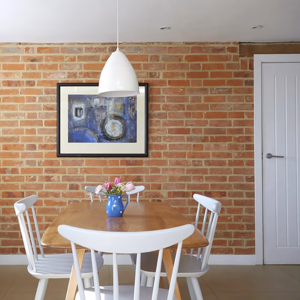 A white dining table and chairs in front of a red brick wall