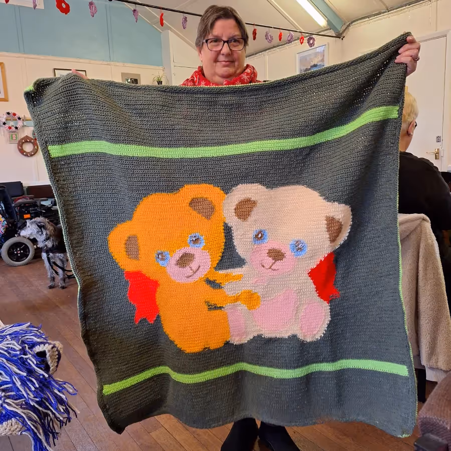 A lady holding a knitted blanket depicting two teddy bears