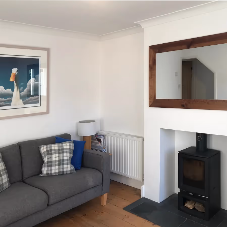 A neutral living room with a grey sofa and wood burning stove