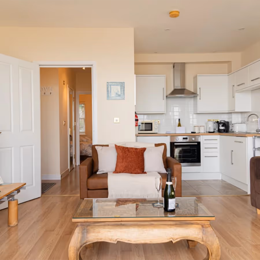 A living room with modern furniture anda white kitchen beyond