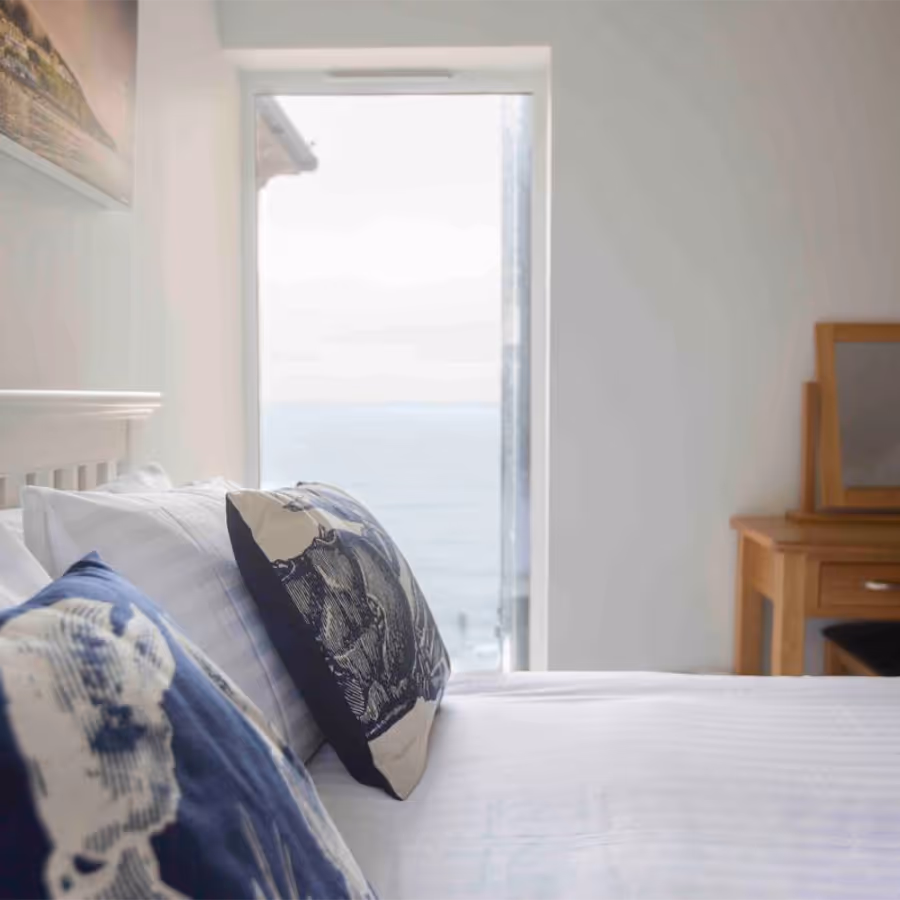 A white and blue bedroom with a door looking out to sea