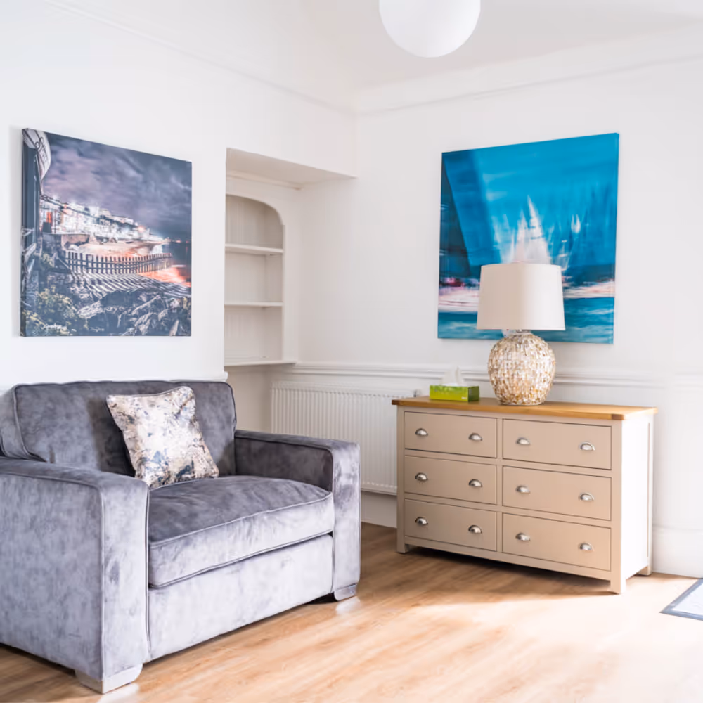 A white living room with a modern grey armchair and teal accents