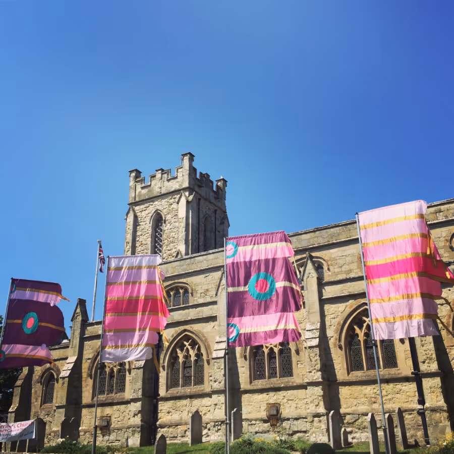 A row of large pink and purple festival flags outside a church