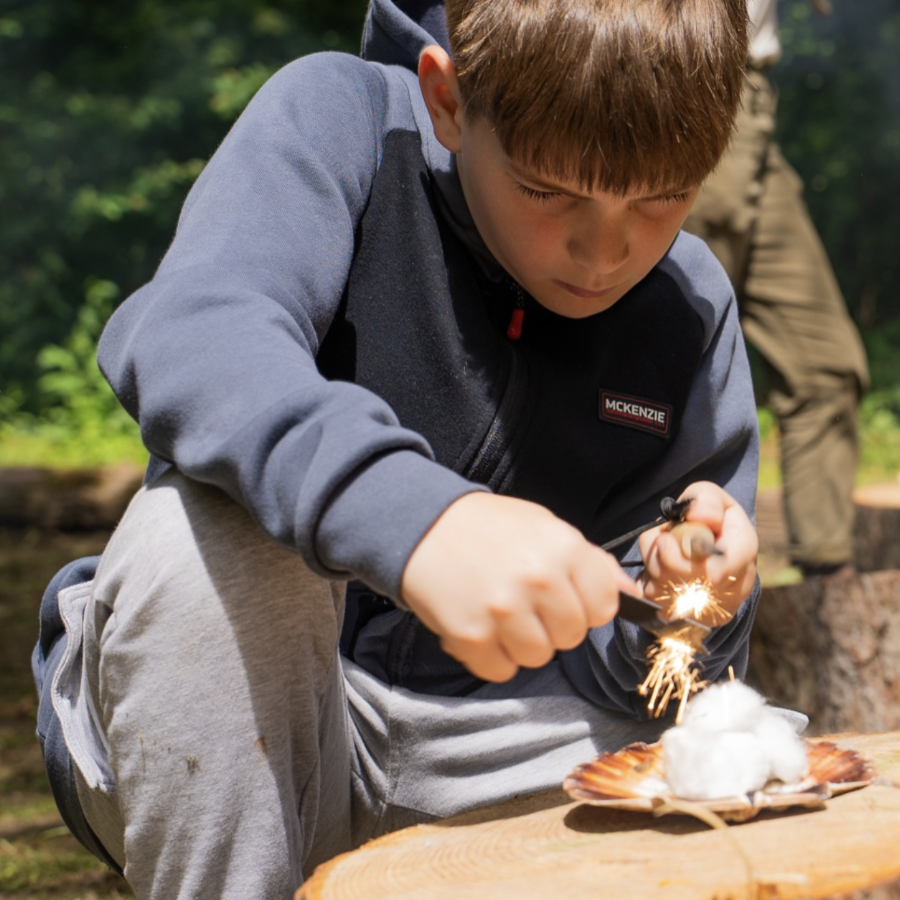 A boy leaning to light a fire using flint