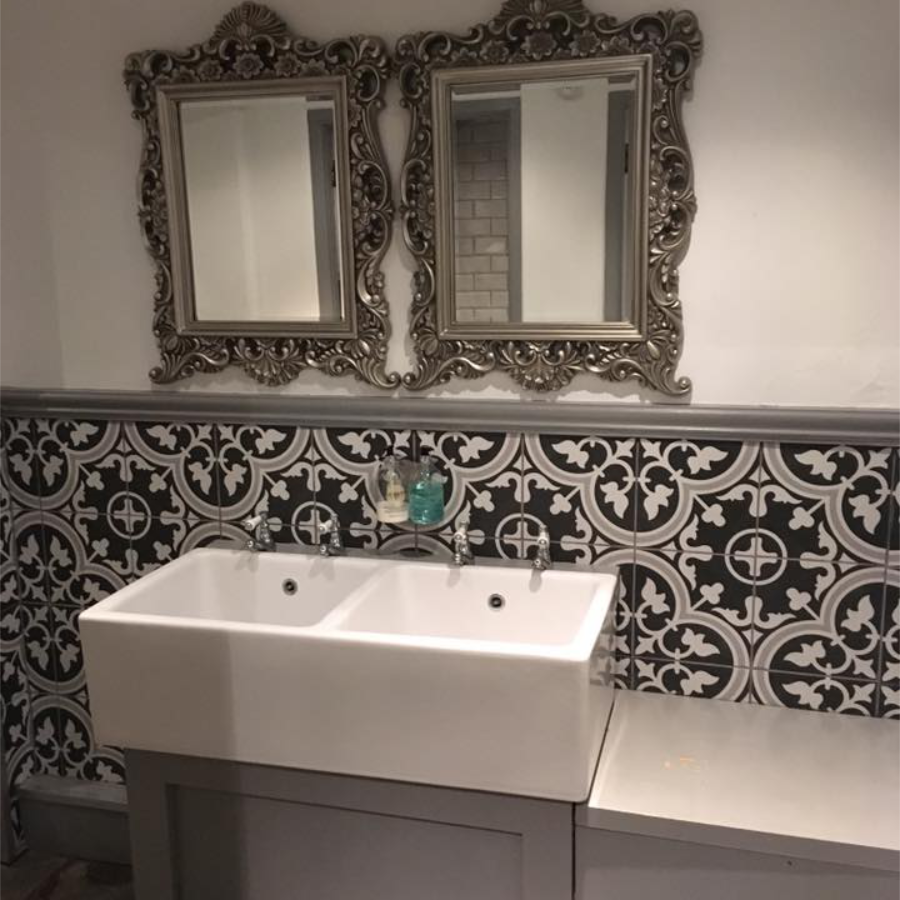 A double basin in a bathroom with black and white tiles and ornate silver mirrors