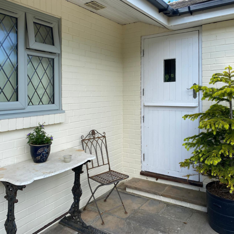 Front entrance to a cream house with sage green windows and a white stable door