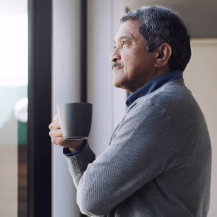 A man holding a mug of coffee, looking out a window.