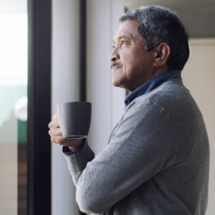 A man holding a mug of coffee, looking out a window.
