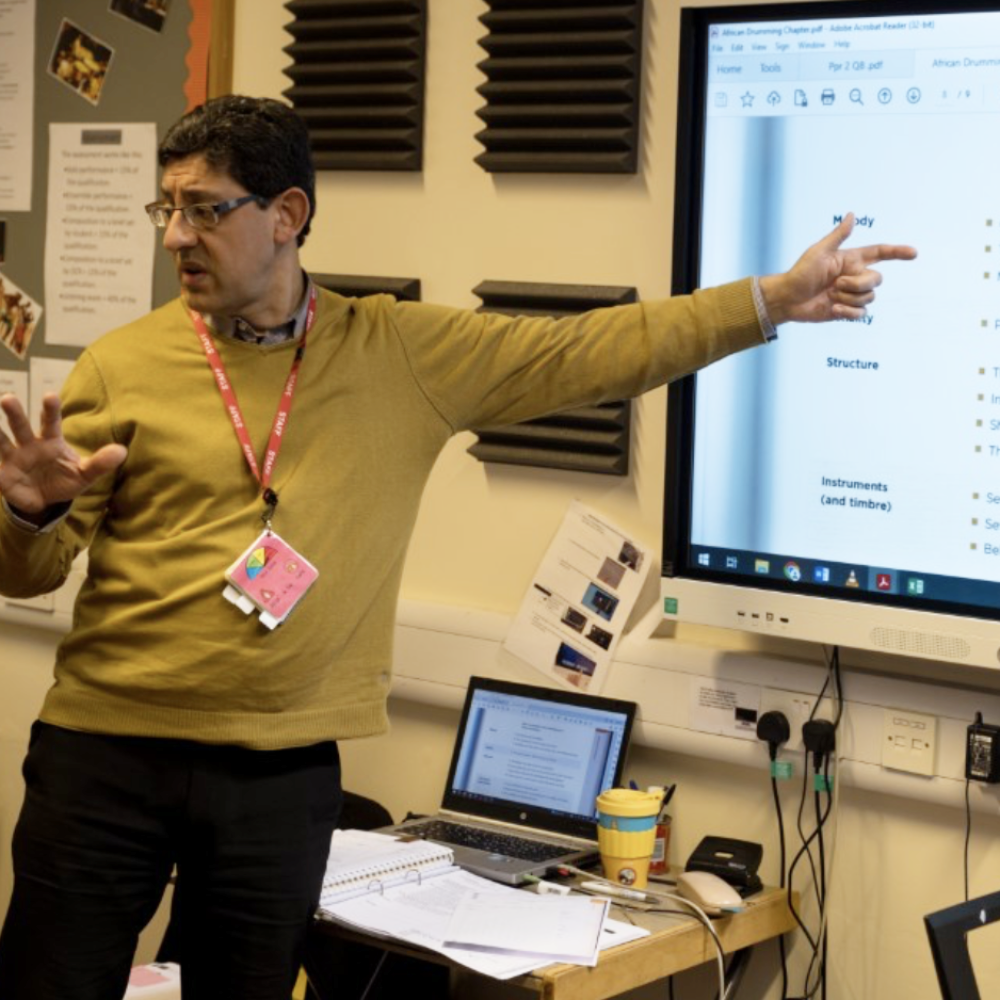 A teacher talking while pointing at a screen