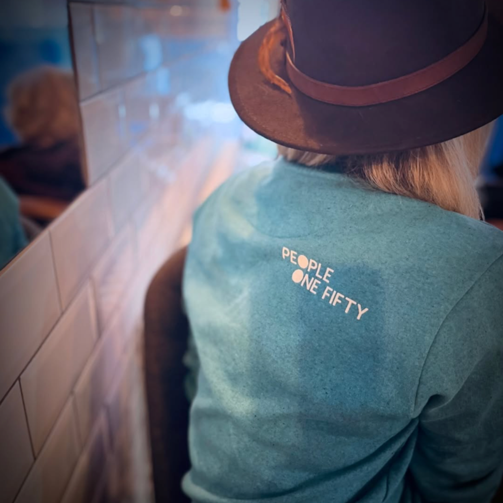 A woman wearing an aqua sweatshirt and a brown hat.
