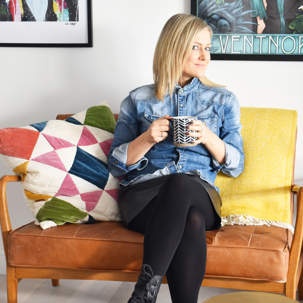 A woman in a denim shirt sitting on a brown sofa.