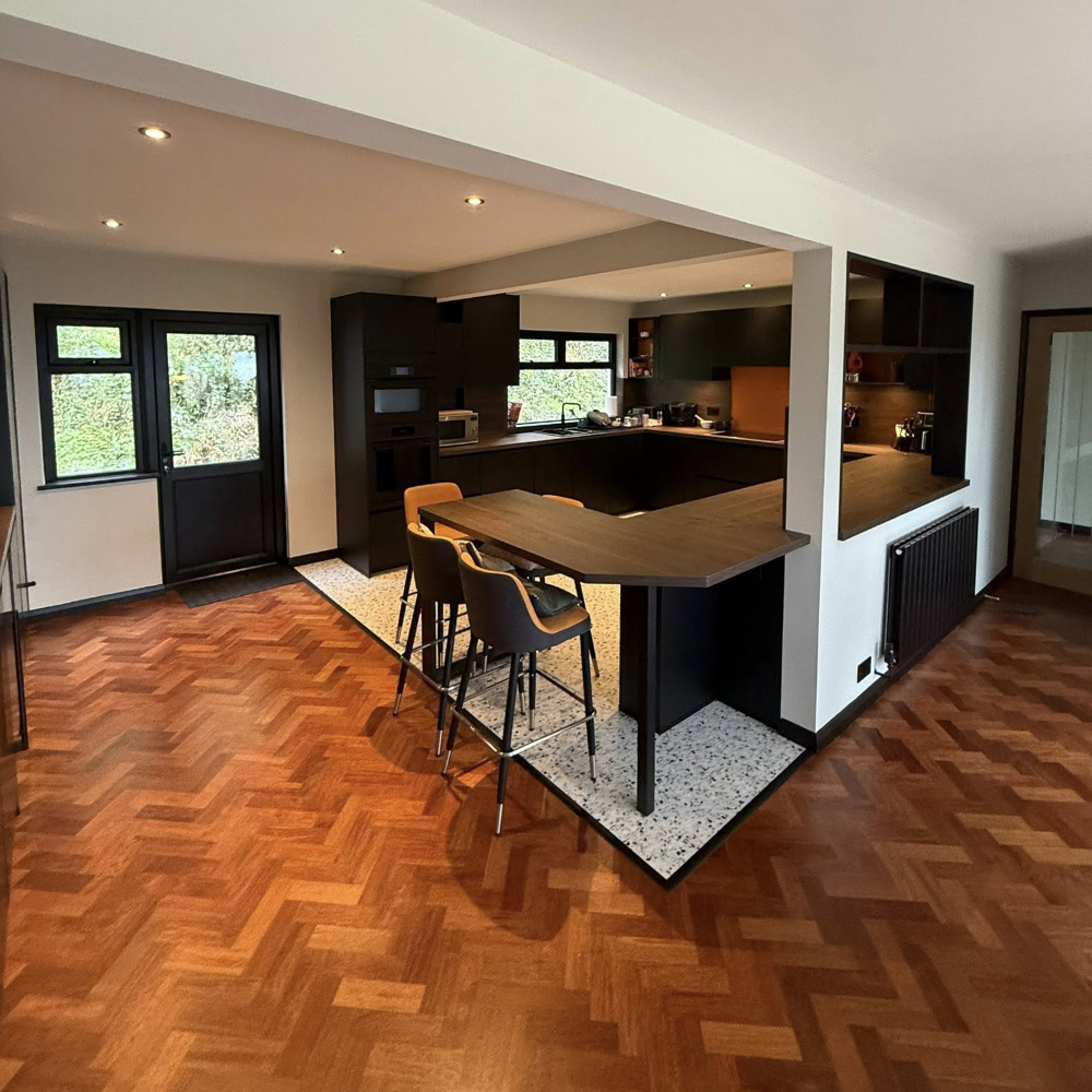 A modern black kitchen with a parquet floor.