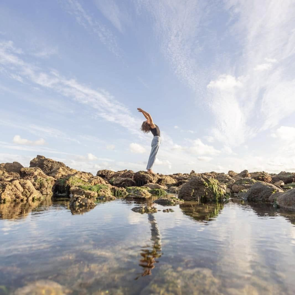 A lady practicing yoga on a beach.