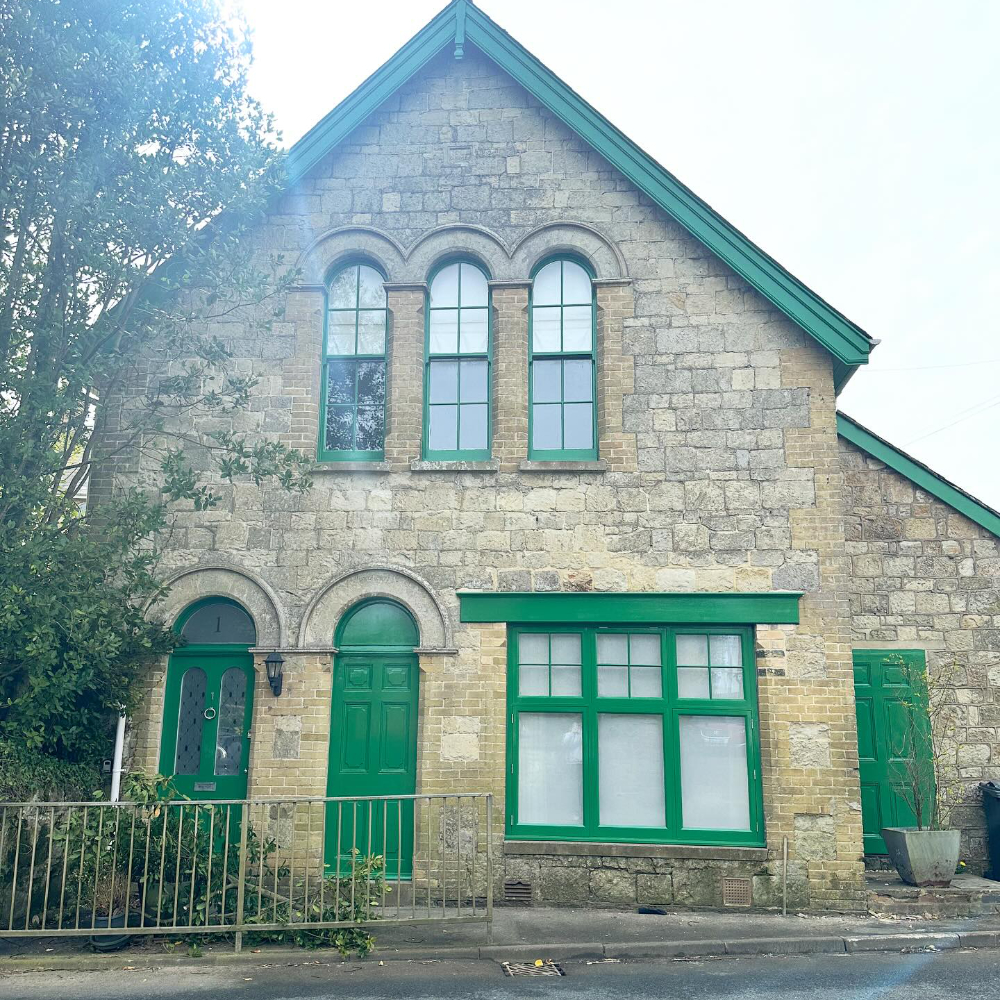 The exterior of a period stone property with windows and doors painted grass green.