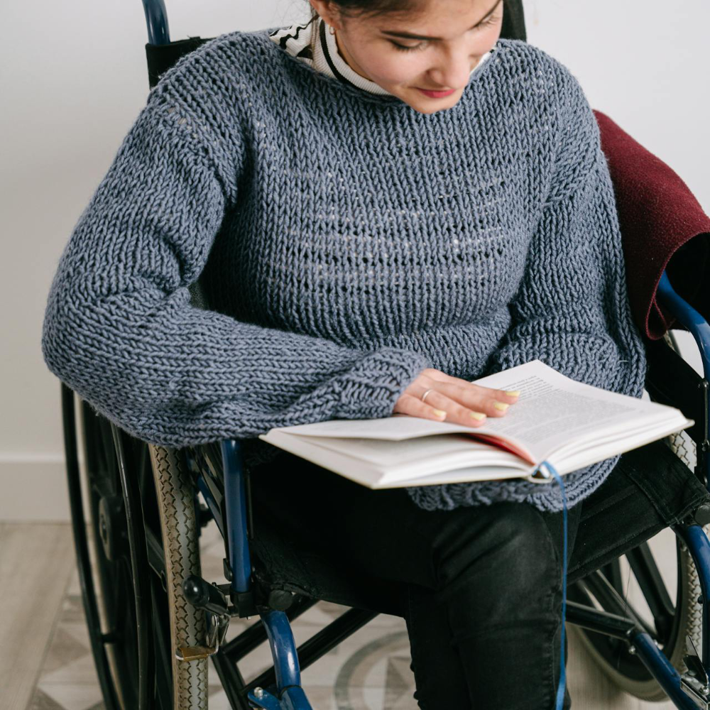 A lady in a wheelchair reading a book.