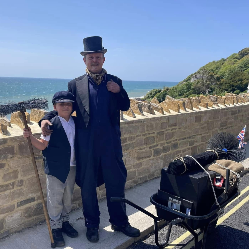 A man and a boy dressed as Victorian chimney sweeps.