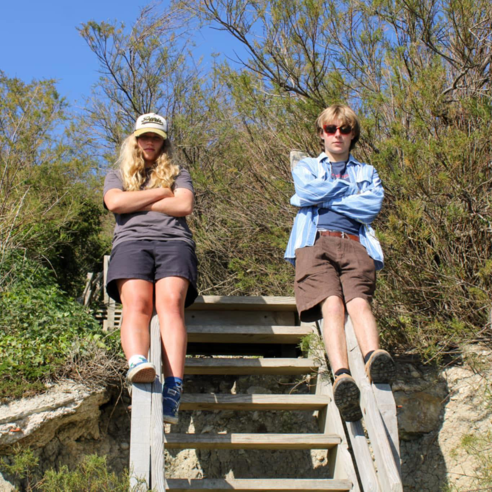 A young man and woman sitting on the handrail of some wooden steps.