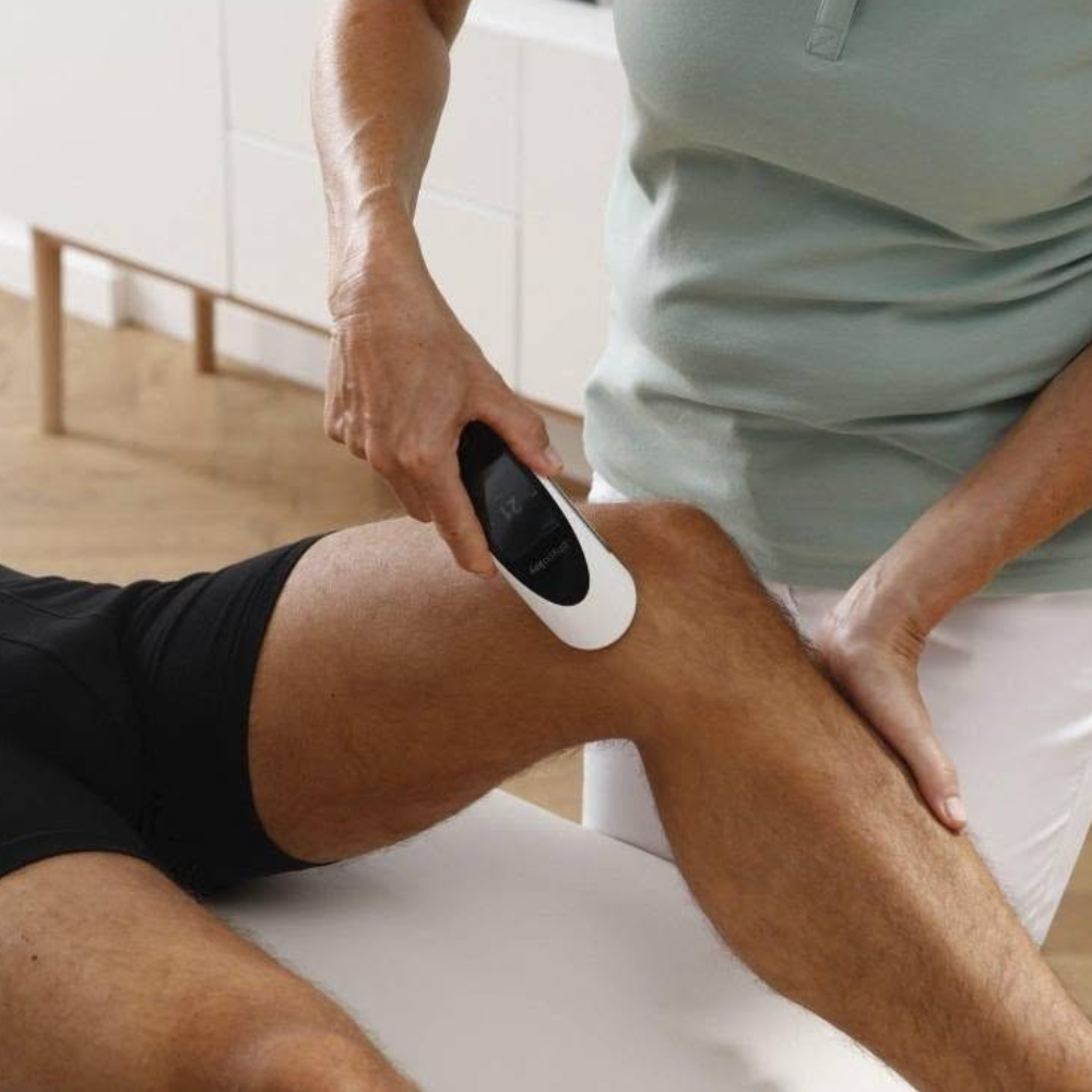 A therapist using a pain relief device on a man's knee.