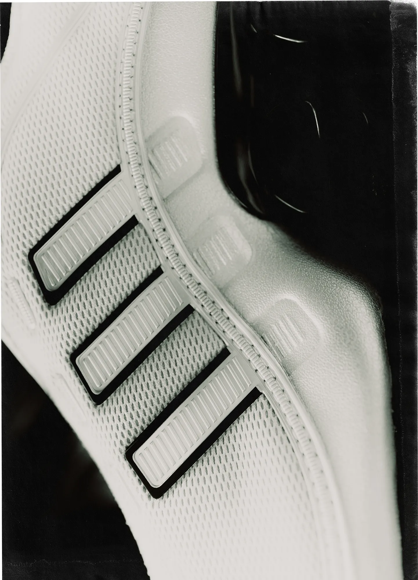 Close-up black-and-white detail of an Adidas sneaker, focusing on the textured mesh upper and the three stripes, with soft motion blur along the sole that suggests movement and cushioning.