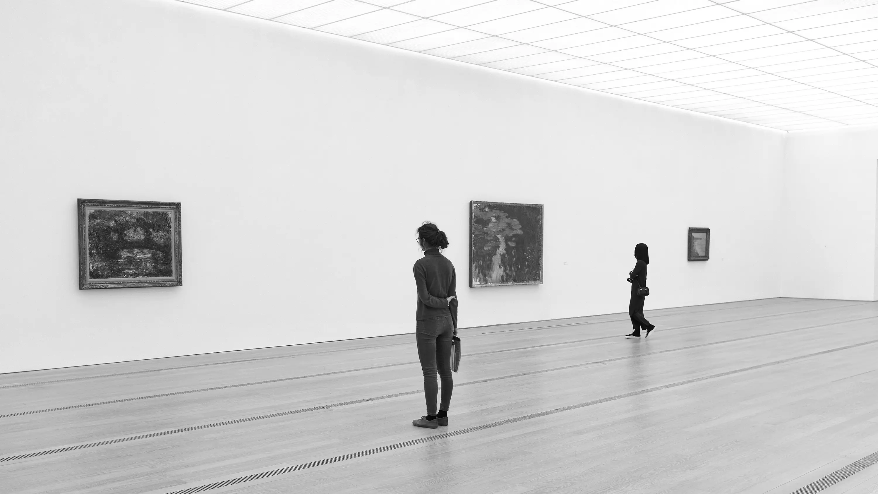 People viewing framed artworks in a bright gallery, black and white