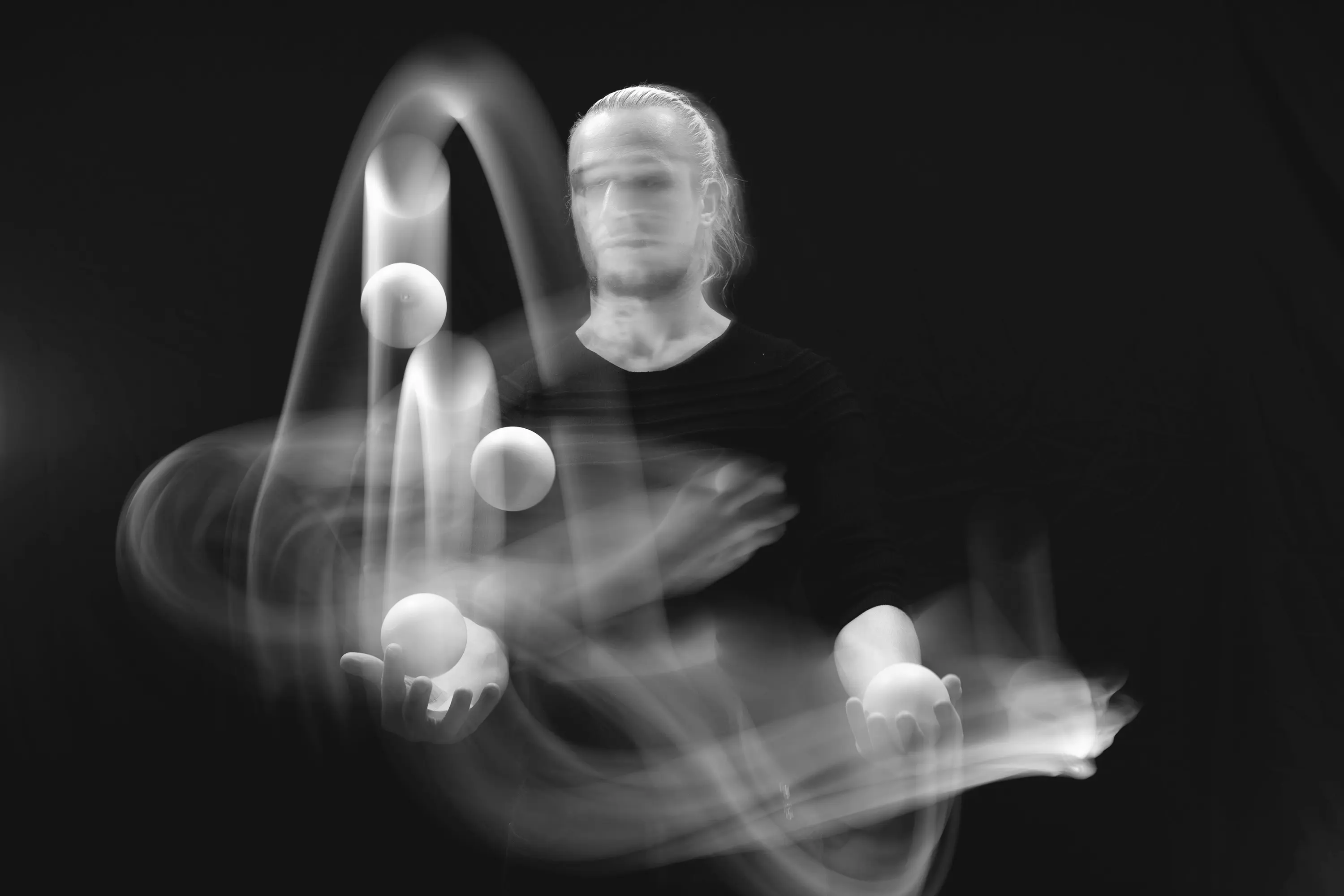 A juggler with motion-blurred juggling balls in mid-air, black and white